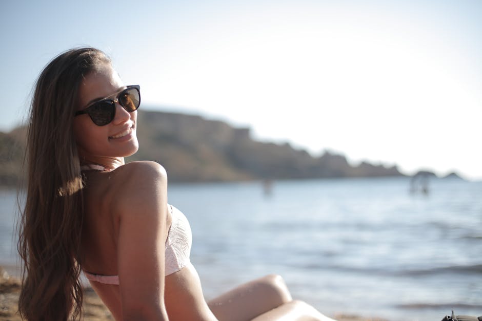 Smiling woman enjoying a sunny beach day wearing sunglasses and a bikini.