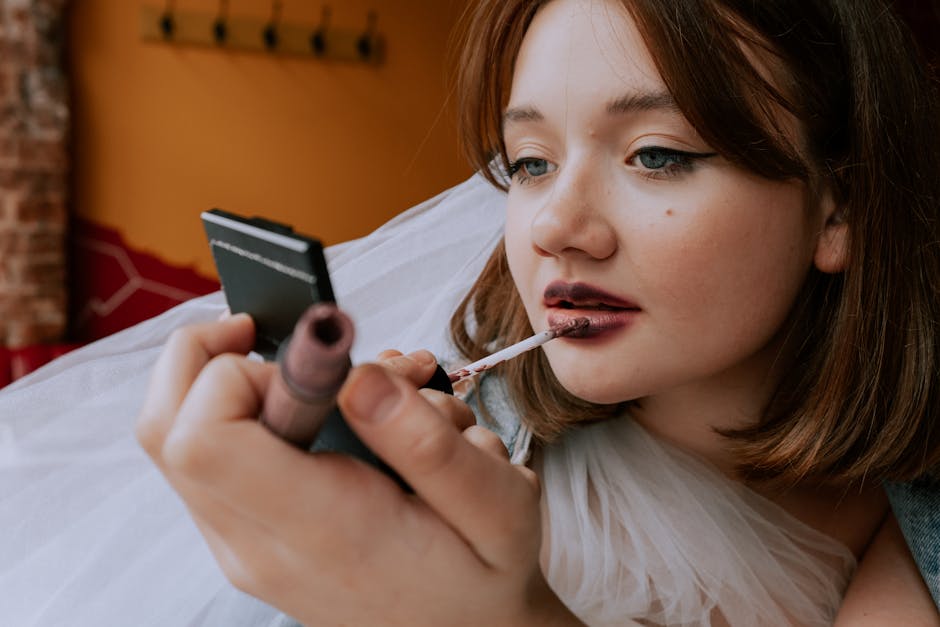 Close-up of a teenager applying lipstick using a hand mirror, indoors.
