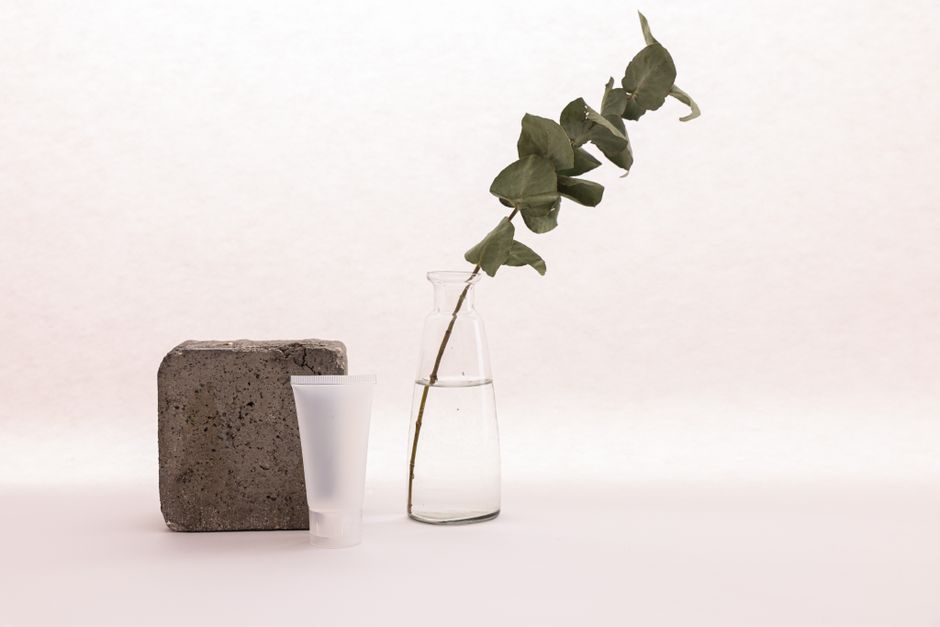 A minimalist composition of skincare tube with a plant and concrete block on a white backd