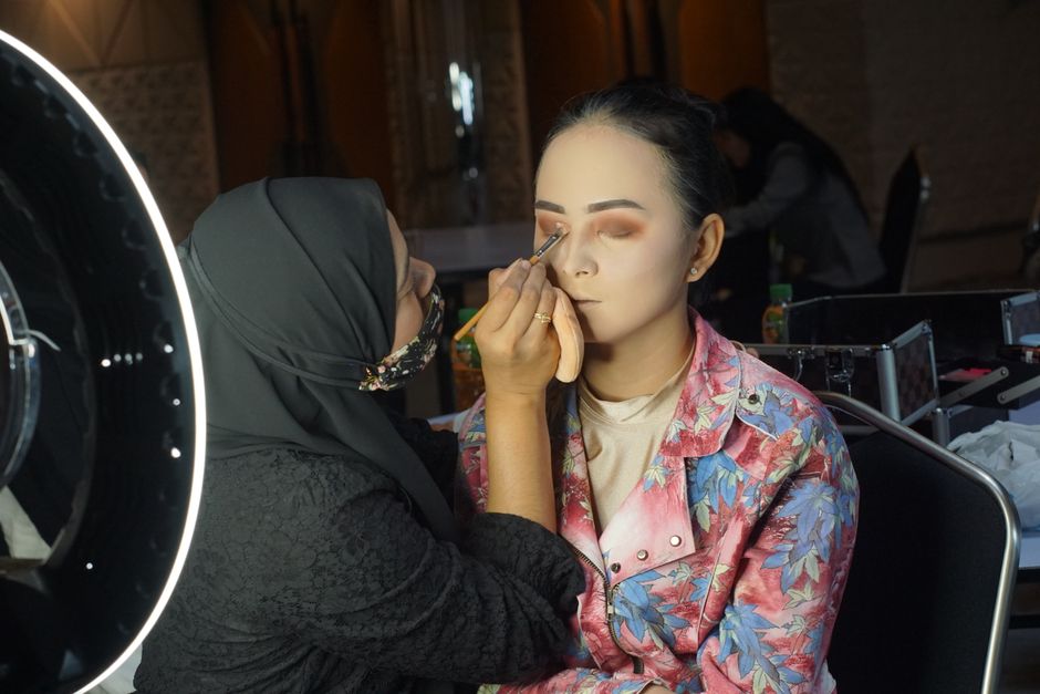 A makeup artist applies eye makeup to a model under bright studio lights during an indoor session.