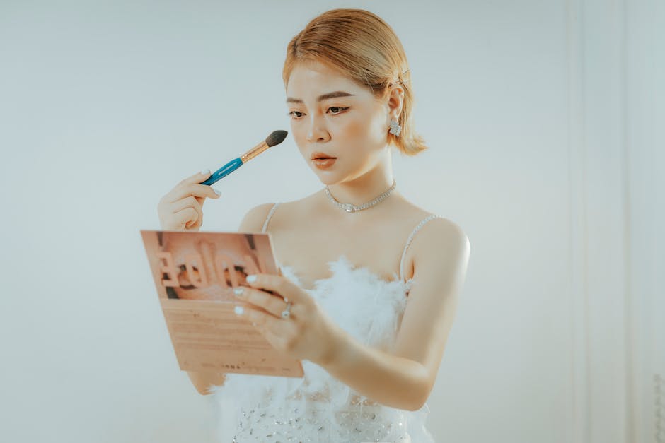 An Asian woman with short hair applies makeup using a brush while looking in a mirror.