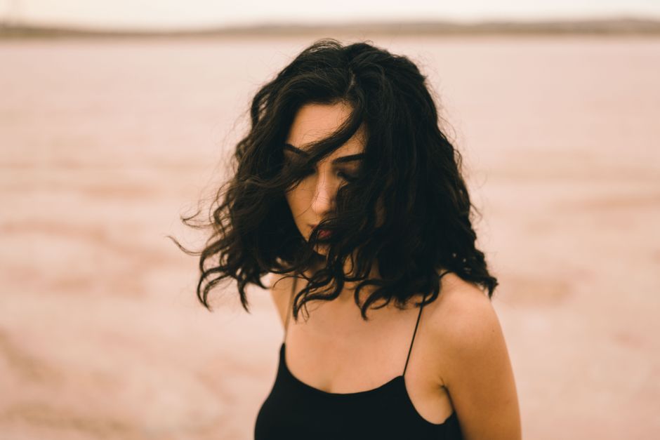 Portrait of a woman with wavy hair standing outdoors, capturing a moody and artistic vibe.