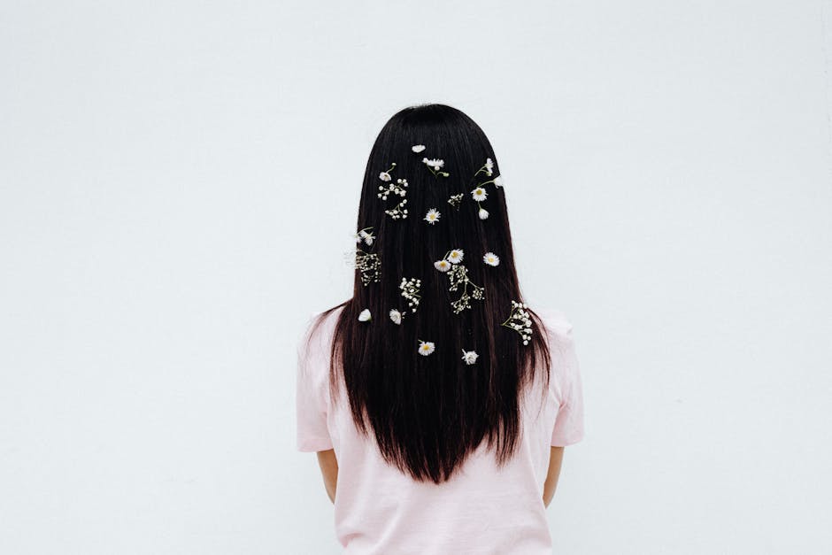 Back view of a woman with long hair adorned with small flowers on a white background.