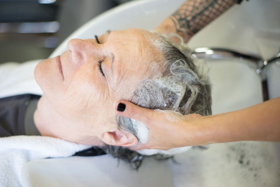 Elderly woman being pampered with a shampoo at a salon, showcasing relaxation and care.
