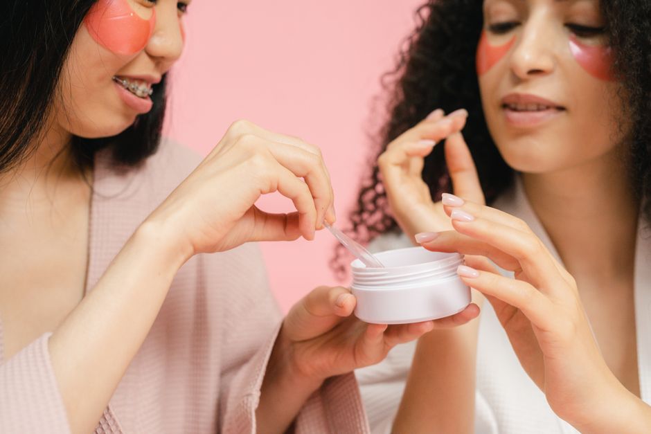 Two women in bathrobes applying skincare products with pink eye masks. Perfect for wellness and beauty themes.