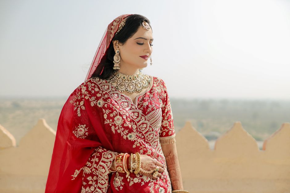 Beautiful Indian bride in red lehenga with intricate jewelry, outdoors.