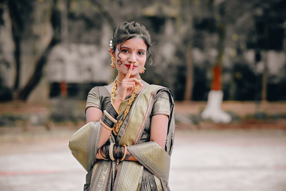 A young woman poses with elegance in a traditional Indian saree, showcasing cultural jewelry outdoors.