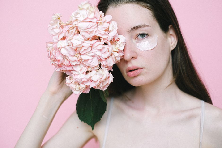 Crop female model with pale skin covered with moisturizing cream standing on pink backgrou