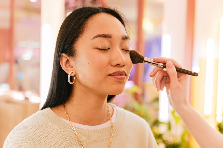 An Asian woman enjoys a makeup session with a brush in a beauty salon setting.