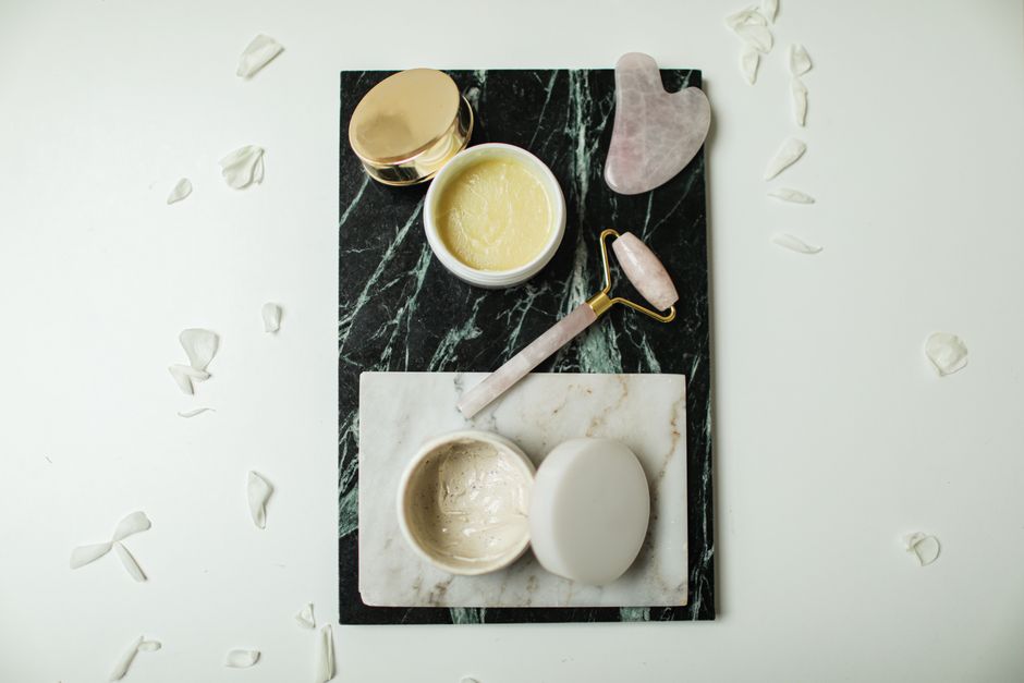Flatlay of luxurious skincare tools and creams on marble slabs, surrounded by flower petal