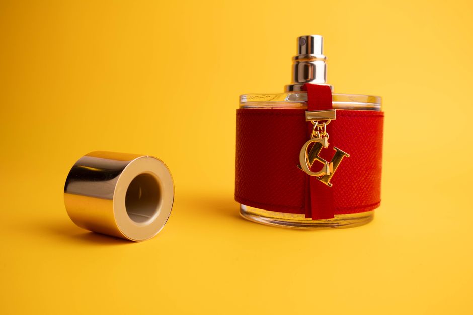 A stylish luxury perfume bottle with a red covering and gold accents against a bright yellow backdrop.