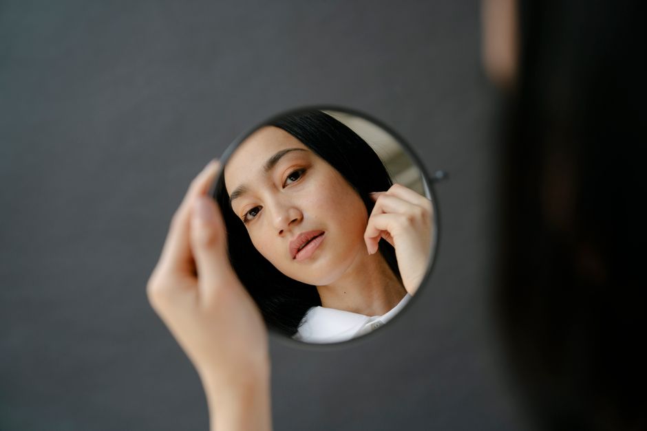 From above of crop attractive Asian female with black hair looking at reflection in round 