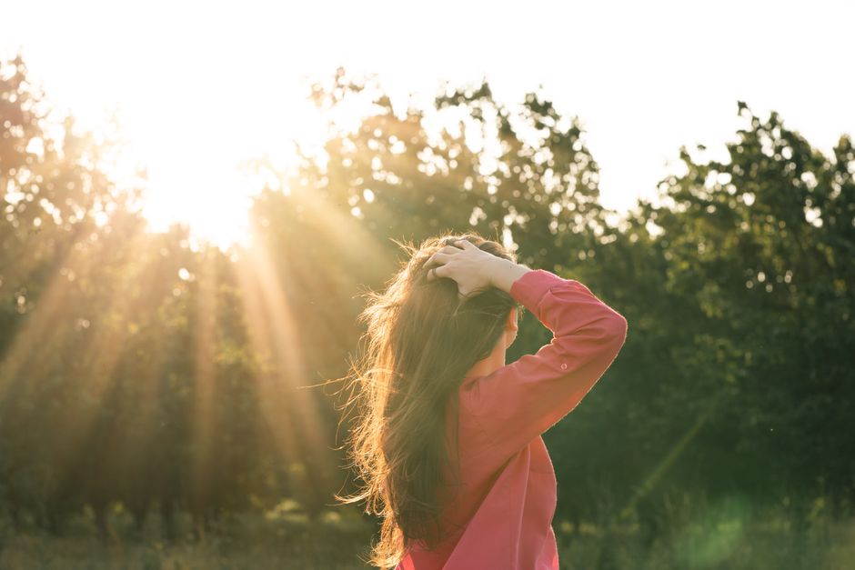 A woman stands in a field bathed in a warm sunset, embracing nature's tranquility.