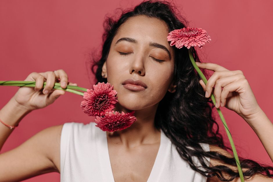 Stylish portrait of a woman with curly hair holding vibrant pink flowers, eyes closed in tranquility.
