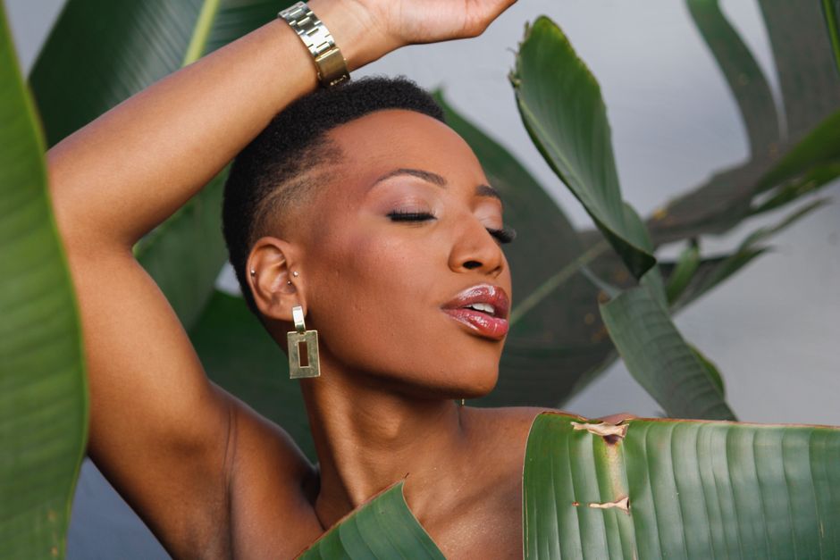 Close-up portrait of a woman with bold earrings and tropical leaves.