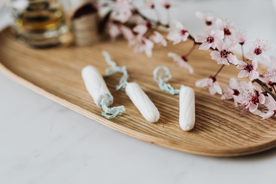 High angle of three menstrual tampons on bamboo plate with flower twig placed against various cosmetic products