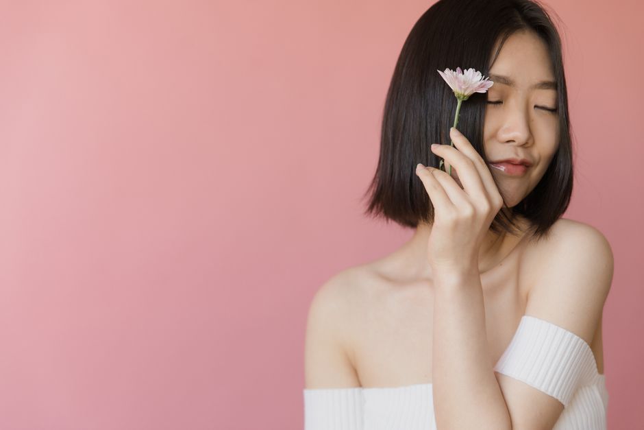 Peaceful portrait of a woman with eyes closed, holding a pink flower against a pink backgr