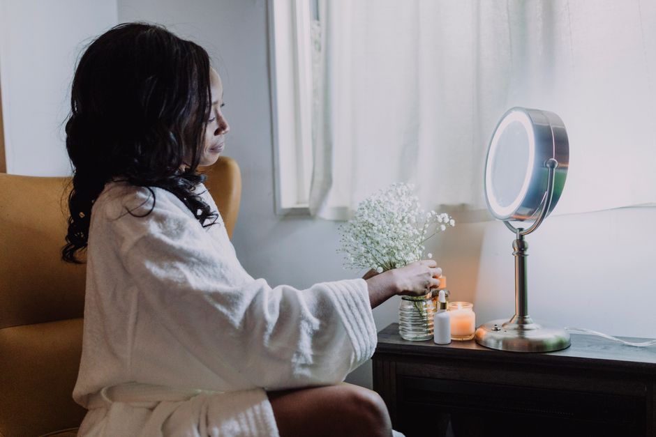 A woman arranges baby's breath flowers by a lit mirror in a warm indoor setting.