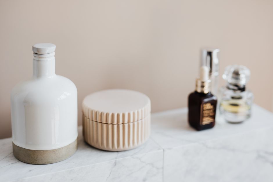Set of reusable cosmetic containers for cream and shampoo arranged near various skincare products and perfume bottle on white marble shelf against beige wall in modern bathroom interior
