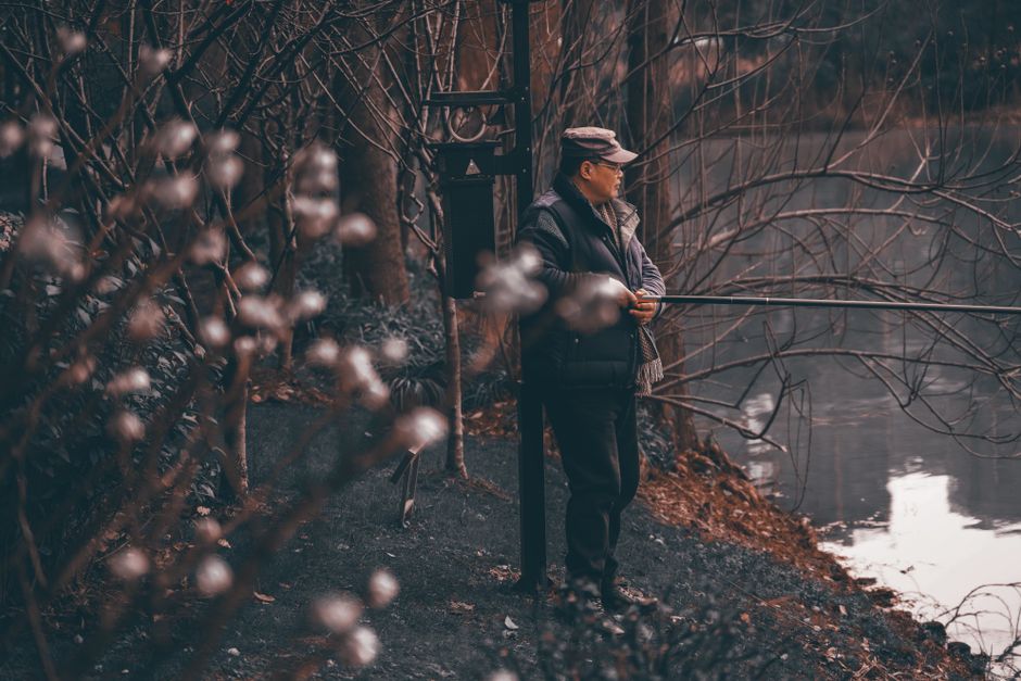 A man in winter attire enjoys a peaceful lakeside view amidst bare trees.