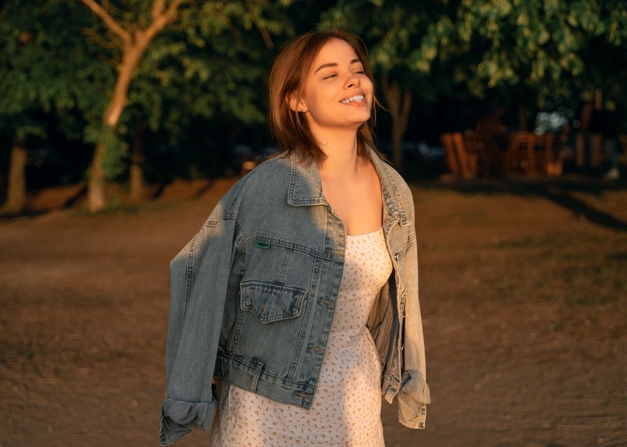 A woman poses delightfully in a denim jacket and dress under the sunset light in Minsk Region, Belarus.