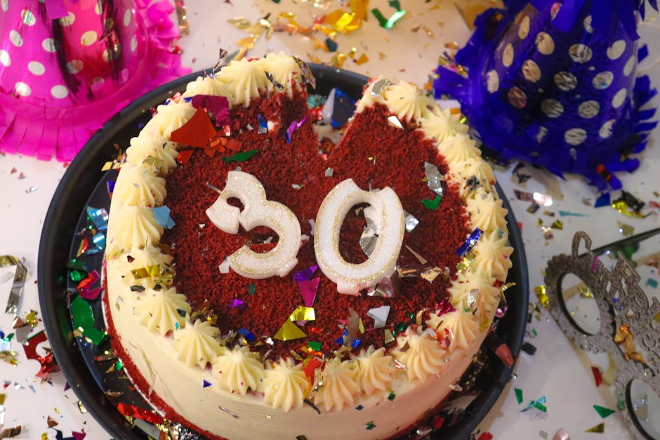 Vibrant red velvet cake with number 30 decoration, surrounded by confetti and party hats.
