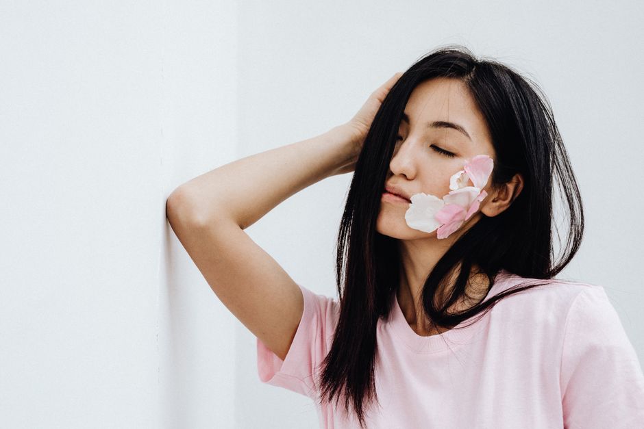 Woman with closed eyes and flower petals on face exuding serenity.