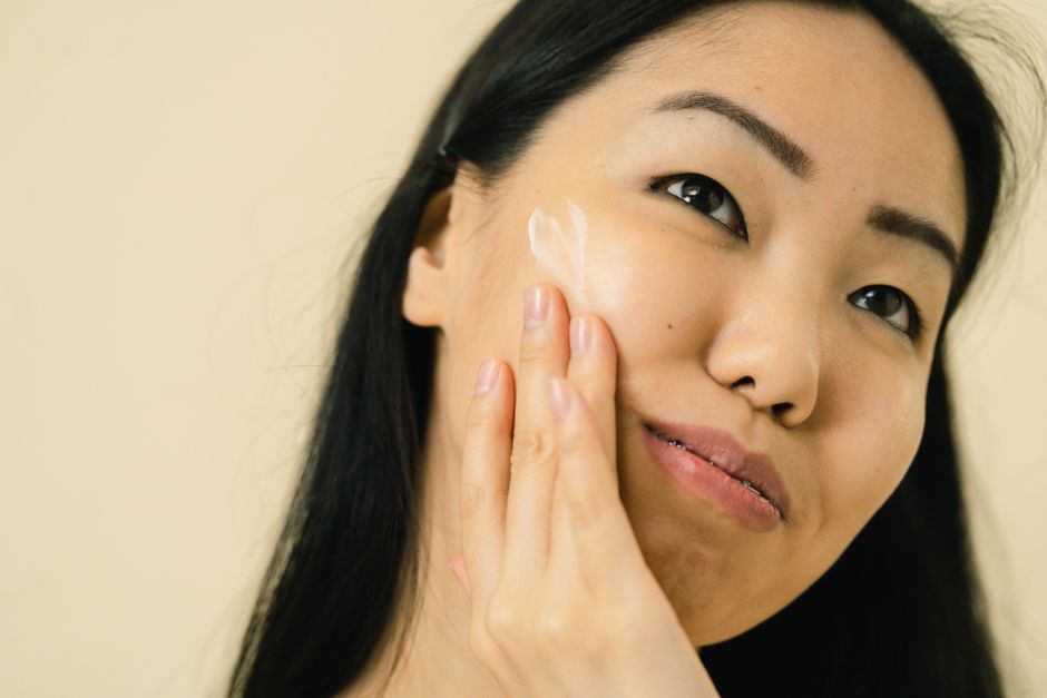 Woman with long black hair applying facial cream in studio. Focus on skincare and beauty r